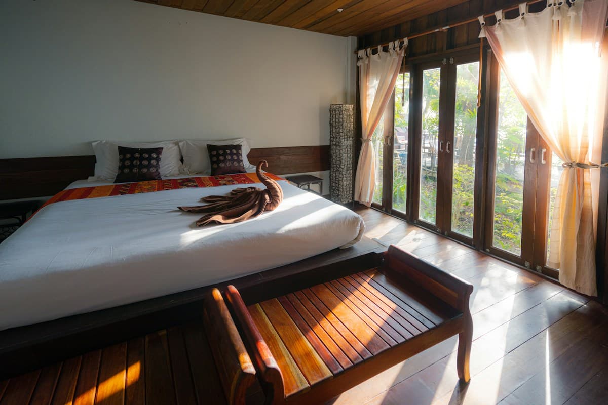 Bright executive room with a wide bed, wooden bench and floor-to-ceiling windows with sheer curtains